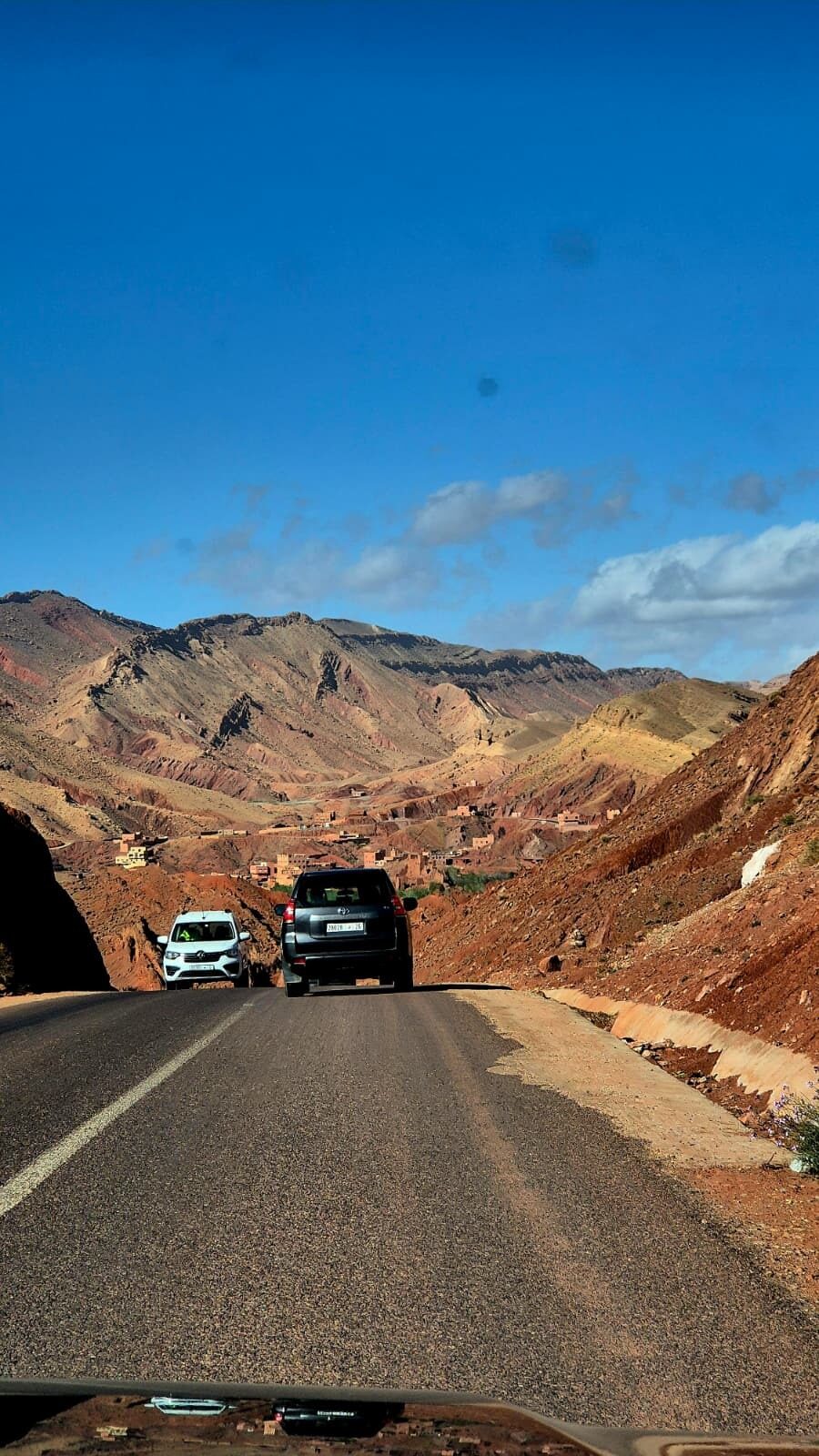 Two cars on a winding mountain road through red hills